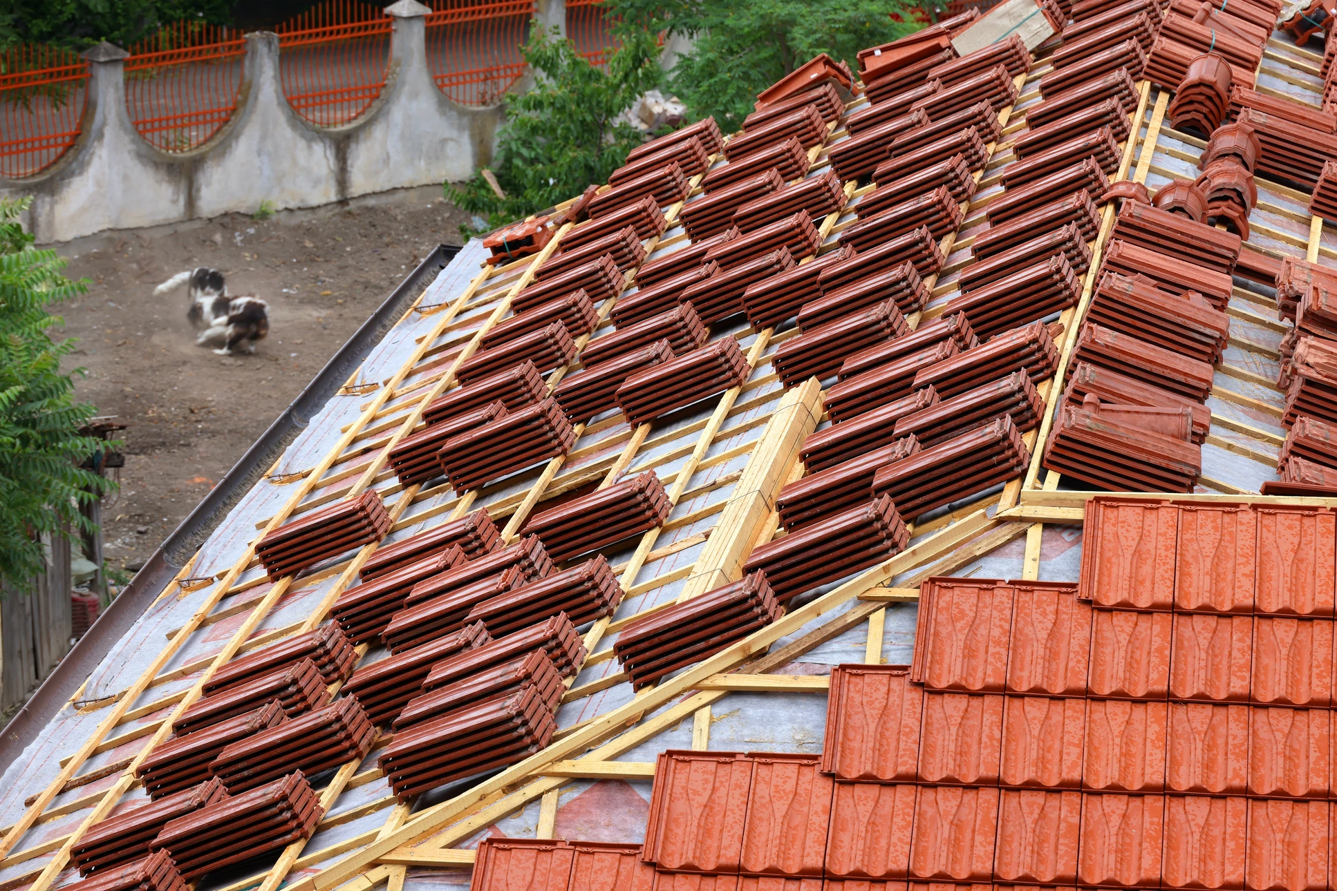 Chantier de couverture en cours avec ouvriers installant des tuiles terre cuite rouge sur charpente bois