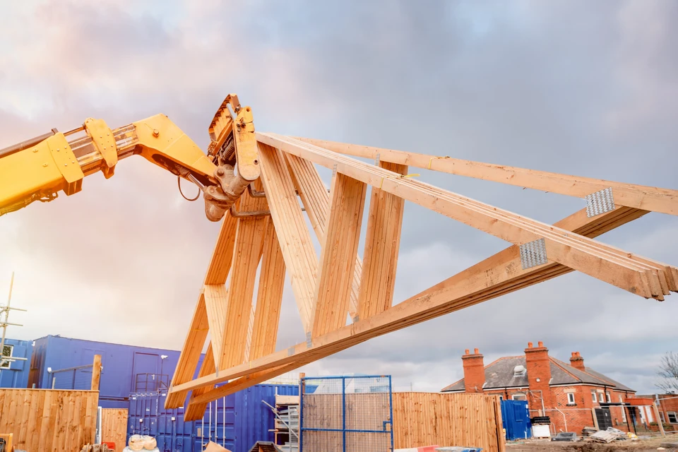 Chantier de construction résidentielle avec grue mobile positionnant une ferme de charpente en bois