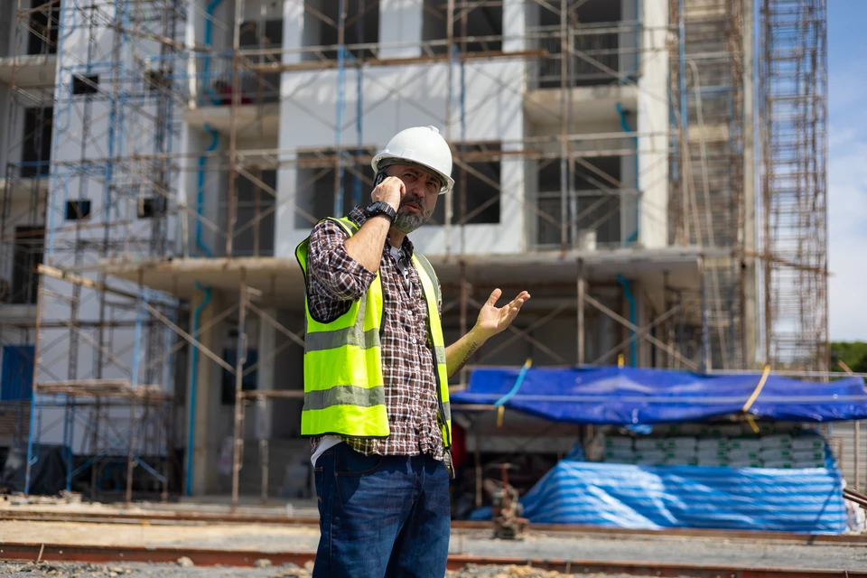 Scène de construction résidentielle montrant plusieurs maisons en cours d'édification avec charpentes bois apparentes, toitures partiellement couvertes et murs en maçonnerie blanche