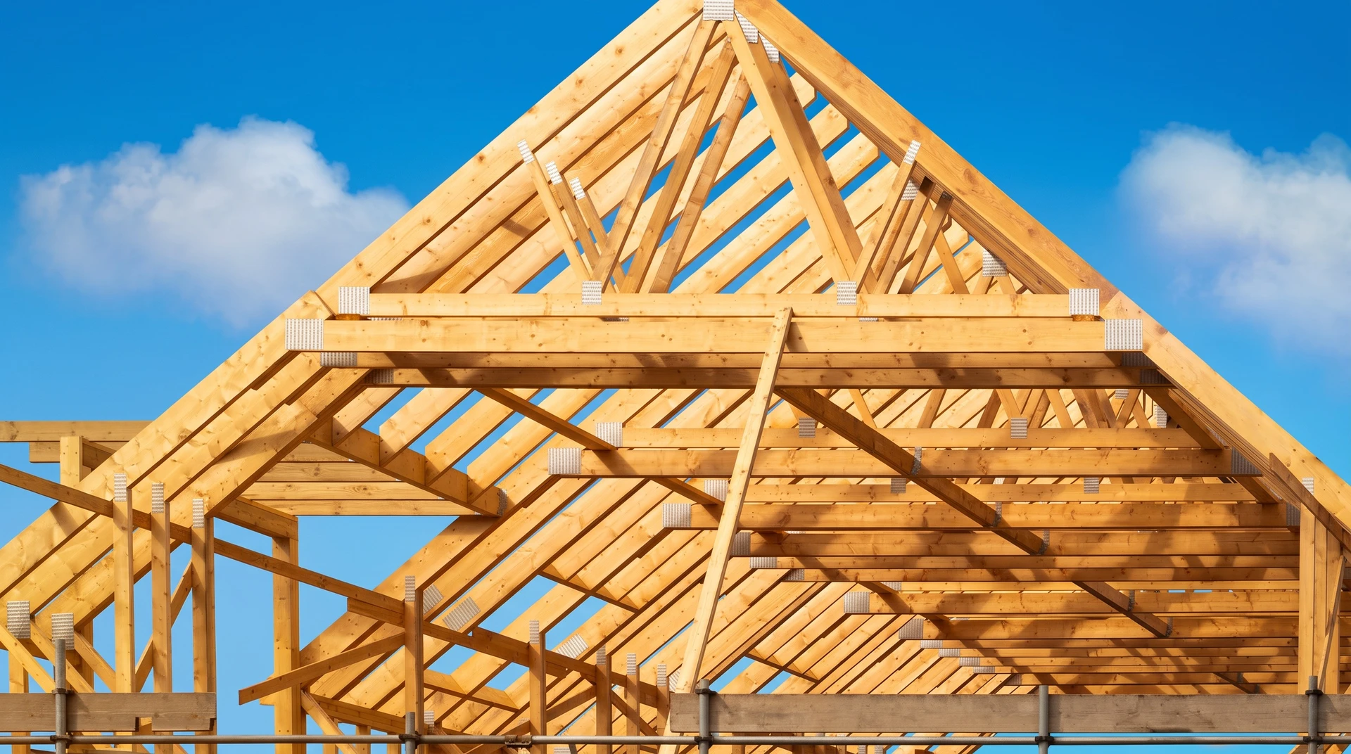 Chantier de construction résidentielle avec grue mobile positionnant une ferme de charpente en bois