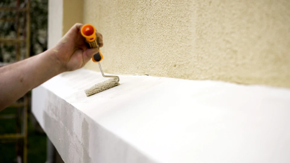 Ouvrier en bâtiment travaillant sur façade extérieure depuis échafaudage, rénovant mur en pierre avec outil de grattage