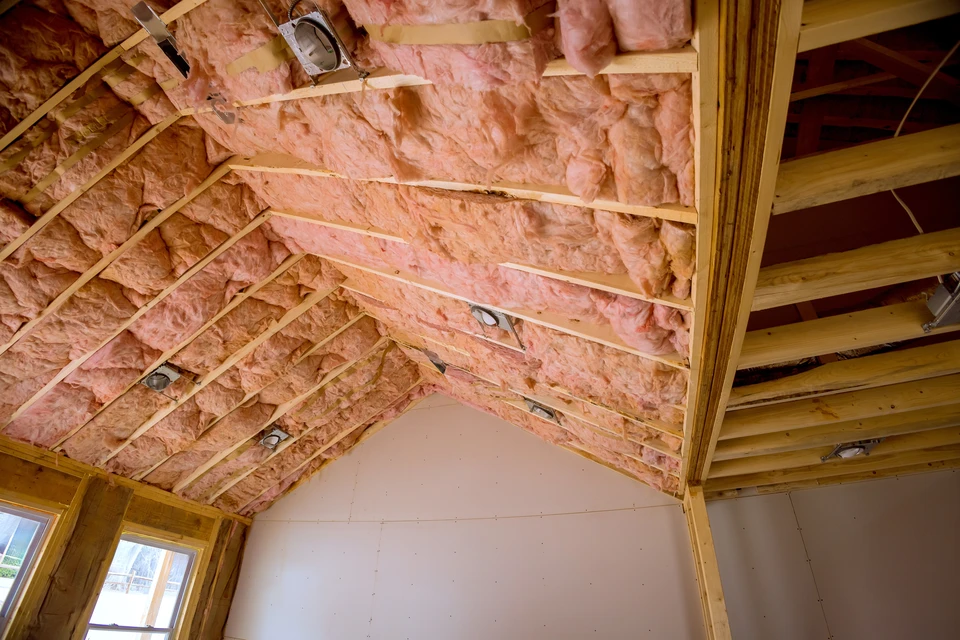 Ouvrier en combinaison bleue installant de l'isolant thermique jaune dans les combles d'une habitation